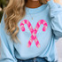 Pink Sequins Candy Canes Patch, a sparkly pink sequin patch in the shape of candy canes crossed in an 'X' design on a light blue sweatshirt.