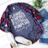Flannels Bonfires Footballs Pumpkins Screen Print Transfer, a casual fall outfit with a graphic t-shirt, plaid shirt, ripped jeans, and sneakers with a green plant in the background.