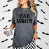 Bad Witch BLACK DTF Heat Transfer, Halloween-themed black text with spider webs and stars on a gray t-shirt worn by a woman.
