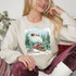 Believe Christmas Train DTF Heat Transfer, a festive design featuring a vintage train, Santa's sleigh with reindeer, snow-covered pine trees, and the word 'Believe' on a Christmas-themed sweatshirt.
