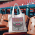 Stings Colorful Mascot DTF Heat Transfer, a vibrant and playful design featuring a smiley face with star-shaped eyes, placed on a white tote bag, outdoors on stadium seating.