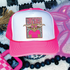 Steers Colorful Mascot DTF Heat Transfer, a pink and white trucker hat with a badge featuring a cartoon steer wearing star-shaped sunglasses and a pink shirt, surrounded by decorative elements.