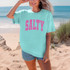 Distressed Salty PINK DTF Heat Transfer, pink distressed text on a turquoise T-shirt worn by a woman on the beach.