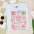 Faux Glitter He Is Risen Floral Cross DTF Heat Transfer, a white T-shirt with a colorful floral cross design and the words "He is risen" in pink.