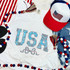 USA Coquette Spangled Transfer, patriotic American-themed apparel including a t-shirt with 'USA' in blue rhinestones, a red, white, and blue trucker hat with an American flag patch, and red, white, and blue bead necklaces.