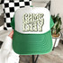 Green Checker Game Day Coquette DTF Heat Transfer, graphic design of the words 'GAME DAY' in checkered pattern with a bow, on a green and white trucker cap.
