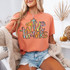 Give Thanks Cross DTF Heat Transfer, colorful and vibrant design of the words "give thanks" with a cross symbol on a woman wearing a peach t-shirt.