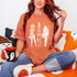 White Halloween Distressed Characters DTF Heat Transfer, product image of white Halloween-themed distressed skeleton and ghost characters graphic on a woman's orange oversized T-shirt.