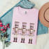 Hand-Painted Pastel Nutcrackers DTF Heat Transfer, pink t-shirt with decorative nutcracker design, blue jeans, beige hat and pink flowers on white background.