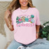 Preppy Home For The Holidays DTF Heat Transfer, colorful festive graphic of holiday houses, Christmas tree, and snowflakes on pink t-shirt.