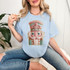 Faux French Knot Nutcracker DTF Heat Transfer, embroidered nutcracker design on a light blue T-shirt, decorative textile artwork featuring a nutcracker with a pink hat and green accents.