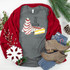 Tis' The Season Christmas Cake Screen Print Heat Transfer, festive graphic on a grey t-shirt with Christmas tree and cake designs, surrounded by holiday decor and clothing items.