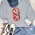 Basketball Number Sequin Patch, red sequined patch with black and white lines resembling a basketball number on a gray sweatshirt worn with distressed jeans and white sneakers.