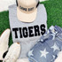 Tigers Fluffy Patch, front view of a starry design patch on denim shorts, beige baseball cap with 'GAME DAY' text, gray sweatshirt with 'TIGERS' in bold letters, white sneakers with brown accents, all arranged on green grass.