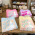Duck Duck Goose DTF Heat Transfer, colorful folded t-shirts with a duck graphic and striped background on display in a retail store.