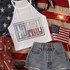Howdy Spangle Heat Transfer, patriotic summer fashion flat lay with American flag-themed tank top, denim shorts, cowboy boots, small American flag, and sparker against United States flag background.