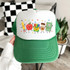 School Doodles DTF Heat Transfer, colorful cartoon school supplies characters on white and green cap, including a pencil, apple, crayon box, coffee cup, and notebook.