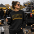 Iowa Football Laces Embroidered Chenille Patch, close-up view of a woman wearing a black sweatshirt with the Iowa logo and football laces embroidery, at a tailgate event.