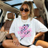 You're Killing Me Smalls Checkered Bolt DTF Heat Transfer, a colorful graphic design featuring a lightning bolt with pink text on a white T-shirt worn by a smiling woman sitting inside a car