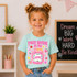 Is My Jam Back to School DTF Heat Transfer | Grades Pre-K–4, a young girl wearing a mint green T-shirt with a pink jam jar graphic and the text "First Grade Is My Jam", smiling at the camera.