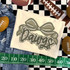 Camo Bow School Mascot DTF Heat Transfer, camouflage bow design with the word 'Dawg' on a white fabric shirt, surrounded by football-themed items.