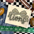Camo Bow School Mascot DTF Heat Transfer, beige fabric with a camo bow and the word 'Lions' in stylized script, surrounded by football-themed items.