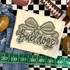 Camo Bow School Mascot DTF Heat Transfer, a design featuring a bow with the word 'bulldogs' in a decorative script, placed on a fabric background with football-themed decor.