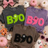 BOO Neon Pink Fluffy Patch, colorful Halloween-themed T-shirts with spooky face patches, surrounded by pumpkins, ghost decorations, candy, and Halloween accessories.
