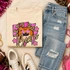 Pink Glitter Mascot - 62 teams - DTF Heat Transfer, colorful graphic design displayed on a beige sweatshirt with distressed denim jeans nearby.