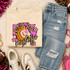 Pink Glitter Mascot - 62 teams - DTF Heat Transfer, displayed on a beige sweatshirt with a colorful mustang graphic and text design, laid out on a soft surface surrounded by casual clothing and accessories.