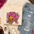 Pink Glitter Mascot - 62 teams - DTF Heat Transfer, close-up of a cream-colored T-shirt with a colorful glitter mascot design surrounded by stars, paired with ripped blue jeans and sneakers.