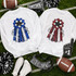Homecoming Mum Sequins Patch - Red, image of two white sweatshirts with sequined homecoming mum patches, one in blue and one in red, laid on a football field with footballs, sneakers, and decorations.