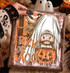 Trick or Moo Highland Cow DTF Heat Transfer, Halloween-themed design featuring a Highland cow with long hair covering its eyes, a pumpkin with a carved face, and spooky background elements.