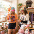 Shop Small Puff Embroidered Hat Patch, two women wearing colorful hats with embroidered patches shopping in a boutique with halloween-themed decorations and trendy clothes.