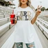 Neutral Marquee Mascot A-P DTF Transfers | School Spirit Mascot Collection, image of a woman holding a Coca-Cola cup and making a peace sign in a stadium with a marquee style mascot design on her white shirt.