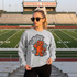 Dotted Mascot DTF Transfers | School Spirit Mascot Collection, a sweatshirt featuring a cartoon tiger mascot with stars around it, worn by a woman standing on a football field.