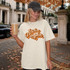 Hey There Pumpkin DTF Transfer, woman wearing a cream t-shirt with the retro fall script design in an outdoor autumn setting.