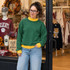 Blank Mockneck Sweatshirt — ROUND 1 EXTRAS, woman wearing green sweatshirt with yellow collar and cuffs, casual style, inside clothing store with sports team apparel in the background.