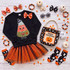 Candy Corn Witch Youth Sequin Patch, a children's Halloween outfit featuring a black sweatshirt with a colorful sequined candy corn witch patch, paired with orange and black striped tulle skirt, Halloween themed accessories including ghost and pumpkin socks, bow hair clips, Halloween jewelry, and a Halloween tote bag on a white wooden background.