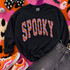 SP00KY appliqué patch transfer with pink, orange and lavender diagonal stripes and black outline pressed on a black sweatshirt