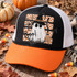 Boo! Halloween DTF transfer with a ghost in a glittery witch hat, broom, spiderweb and spider on an orange-and-white checkered background Shown on a black front panel, orange bill, white mesh back, black rope trucker hat.