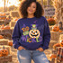 A Tad Bit Wicked Halloween DTF transfer with witch-hatted frog in a striped sweater and bow tie sitting on a checkered jack-o'-lantern pumpkin Shown on a Indigo Blue crewneck sweatshirt.