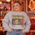 Goosebumps DTF transfer with retro pink and orange television displaying a green monster face as static, dripping chartreuse lettering, and scattered stars Shown on a Ash crewneck sweatshirt.