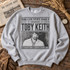 Toby Keith DTF transfer designed as a vintage newspaper front page with distressed photo and 'Should've Been a Cowboy - As Good As I Once Was' headline Shown on a Sport Grey crewneck sweatshirt.