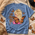 I Will Always Love You DTF transfer featuring an angelic blonde woman with a golden halo, pink outfit, and monarch butterfly wings surrounded by fluttering butterflies Shown on a Mystic Blue t-shirt.