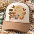 I Will Always Love You DTF transfer with illustrated blonde woman wearing a gold halo and monarch butterfly wings, surrounded by flying butterflies and gold glitter-style splatter Shown on a ivory front panel with camel bill and leopard mesh back trucker hat.