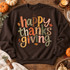 Happy Thanksgiving DTF transfer with colorful patchwork lettering in gingham, plaid, stripes, and polka dot patterns surrounded by fall leaf and berry doodles Shown on a Dark Chocolate crewneck sweatshirt.