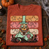 Whimsical pumpkin-headed Mayor DTF transfer in mint top hat and coat with spider brooch, retro stars, and haunted graveyard silhouette Shown on a Brick t-shirt.