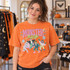 Monster Mash Halloween DTF transfer with retro lettering and dancing mummy, Dracula, Frankenstein's monster, and werewolf characters with bats and starburst doodles Shown on a Bright Orange t-shirt.