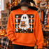 Trick or Treat ghost DTF transfer with jack-o-lantern bag and polka dot background on purple shirt Shown on a Safety Orange crewneck sweatshirt.